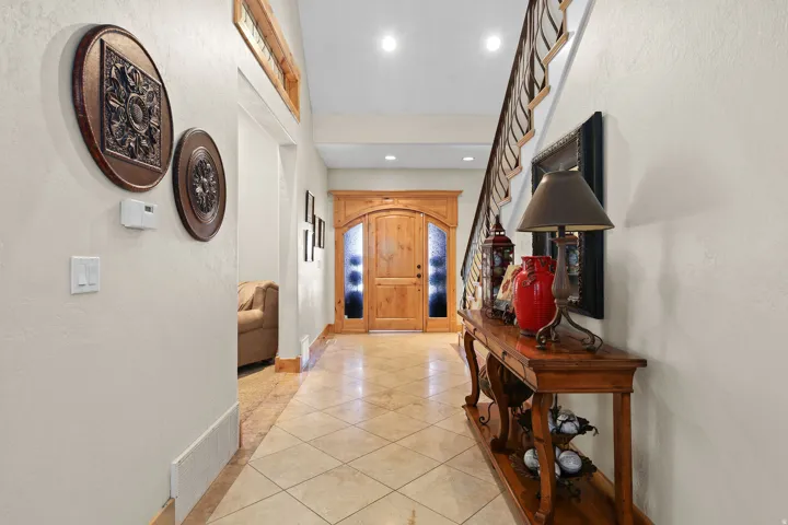 Inviting entryway featuring a wood-finish arched door with frosted glass panels, tile flooring, and a visible staircase with wood newel posts and balusters