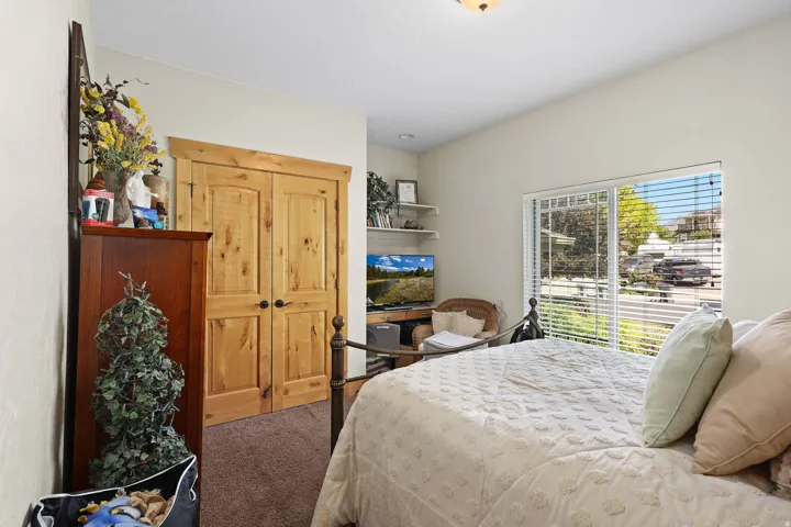 Bedroom featuring natural wood double closet doors, a large window with white blinds, neutral wall paint, recessed shelving, and brown carpeting