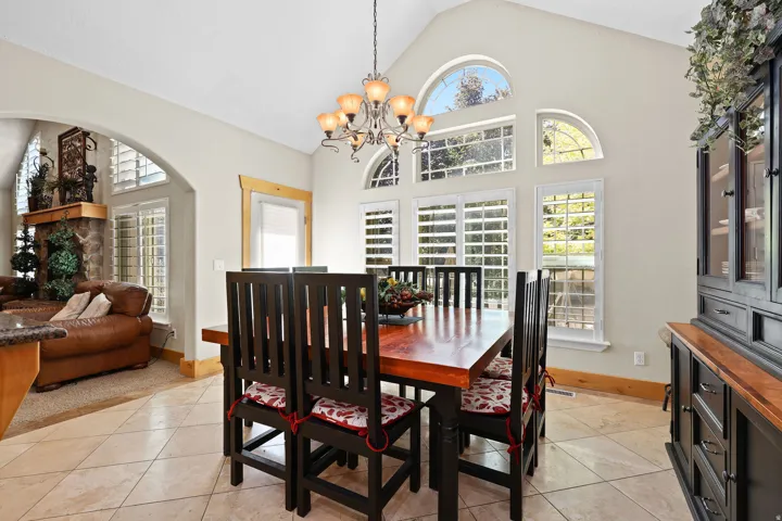 Vaulted ceiling dining area featuring tiled flooring, a decorative chandelier, and a range of arched and rectangular windows
