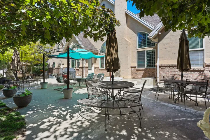 Expansive concrete patio area with a pergola structure and mature trees providing shade