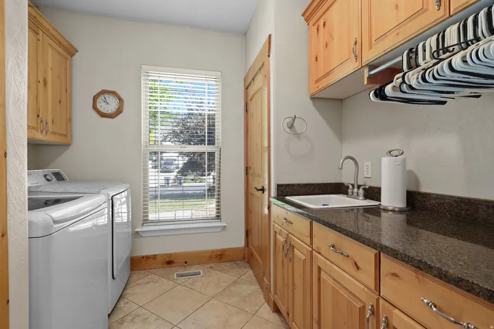 Laundry room featuring light wood cabinetry, a utility sink with a stainless steel faucet, and dark stone-finish countertops