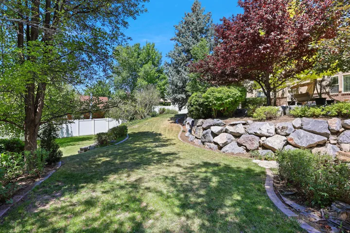 Expansive tiered backyard featuring a natural stone retaining wall, mature trees, and established shrubbery