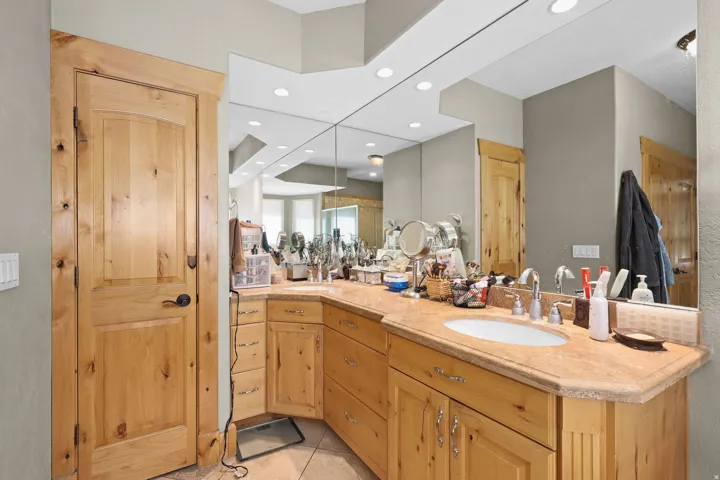 Bathroom featuring a light wood-finish vanity with an integrated sink and light-toned countertop, a full-wall mirror, recessed lighting, and a light wood-finish door with dark hardware