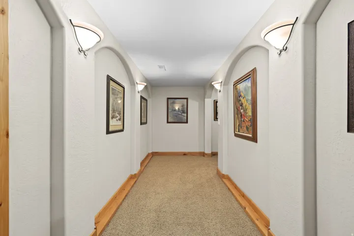 Hallway featuring arched wall recesses, wall-mounted sconces, wood trim, and carpet flooring