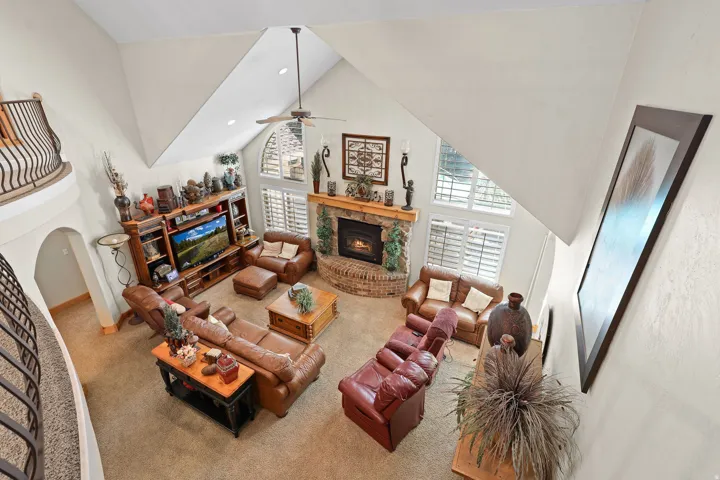 Spacious living area featuring a vaulted ceiling with a ceiling fan, a stone-faced fireplace with a brick hearth, and arched windows with plantation shutters