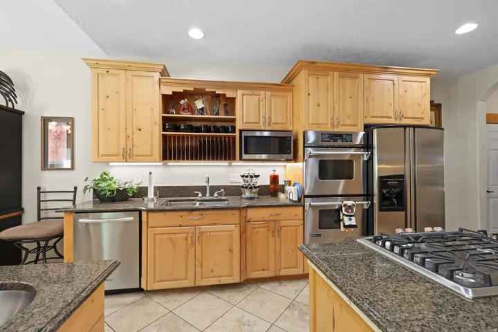 Kitchen featuring wood cabinetry, stainless steel appliances, granite countertops, tile flooring, and integrated sink with an overhead light fixture