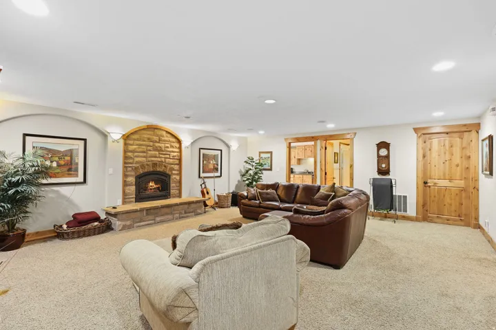 Living area featuring a stone fireplace with hearth, recessed lighting, carpet flooring, a wood-paneled door, and wood-trim double sliding doors