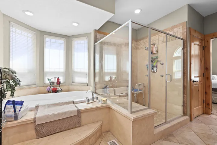 Corner soaking tub with a tiled surround, three bay windows with blinds, and recessed lighting