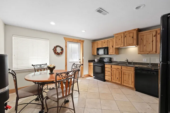 Kitchen featuring wood cabinetry, black appliances, dark countertops, and tile flooring