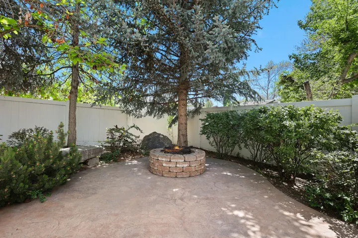 Private backyard patio with a stone fire pit, stamped concrete flooring, mature trees, and a solid privacy fence