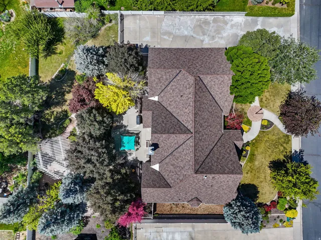 Expansive property featuring a multi-gabled roof, mature landscaping with varied foliage, and a patio with a pergola