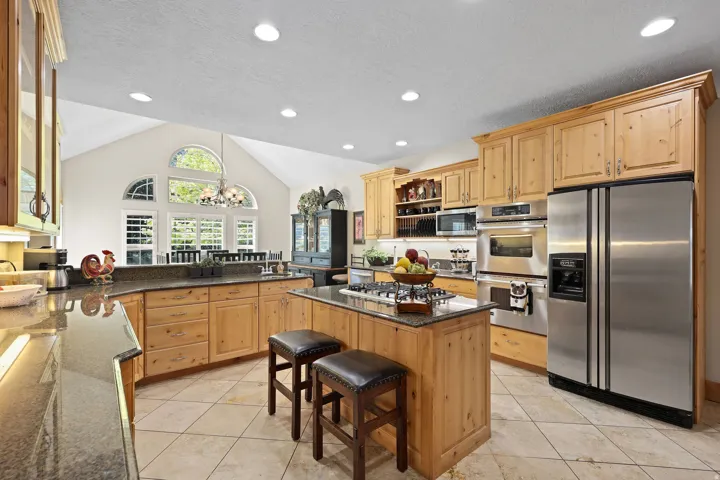 Spacious kitchen featuring natural wood cabinetry, stainless steel appliances, granite countertops, and a central island with a gas cooktop