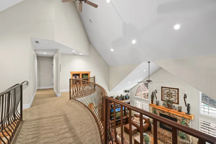 Curved wrought iron railing overlooking a living space with a stone fireplace, vaulted ceiling, and recessed lighting