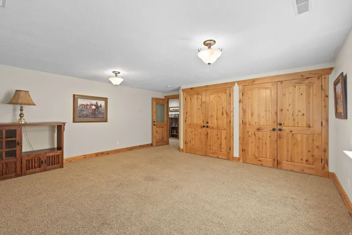Carpeted room featuring natural wood doors with dark hardware, natural wood trim, and cream-colored walls