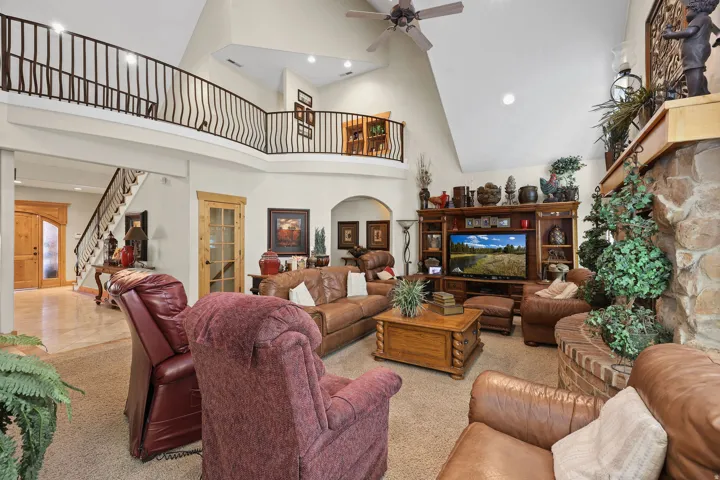 Spacious living area featuring a vaulted ceiling with a fan, a stone fireplace with a wood mantle, and an integrated entertainment center