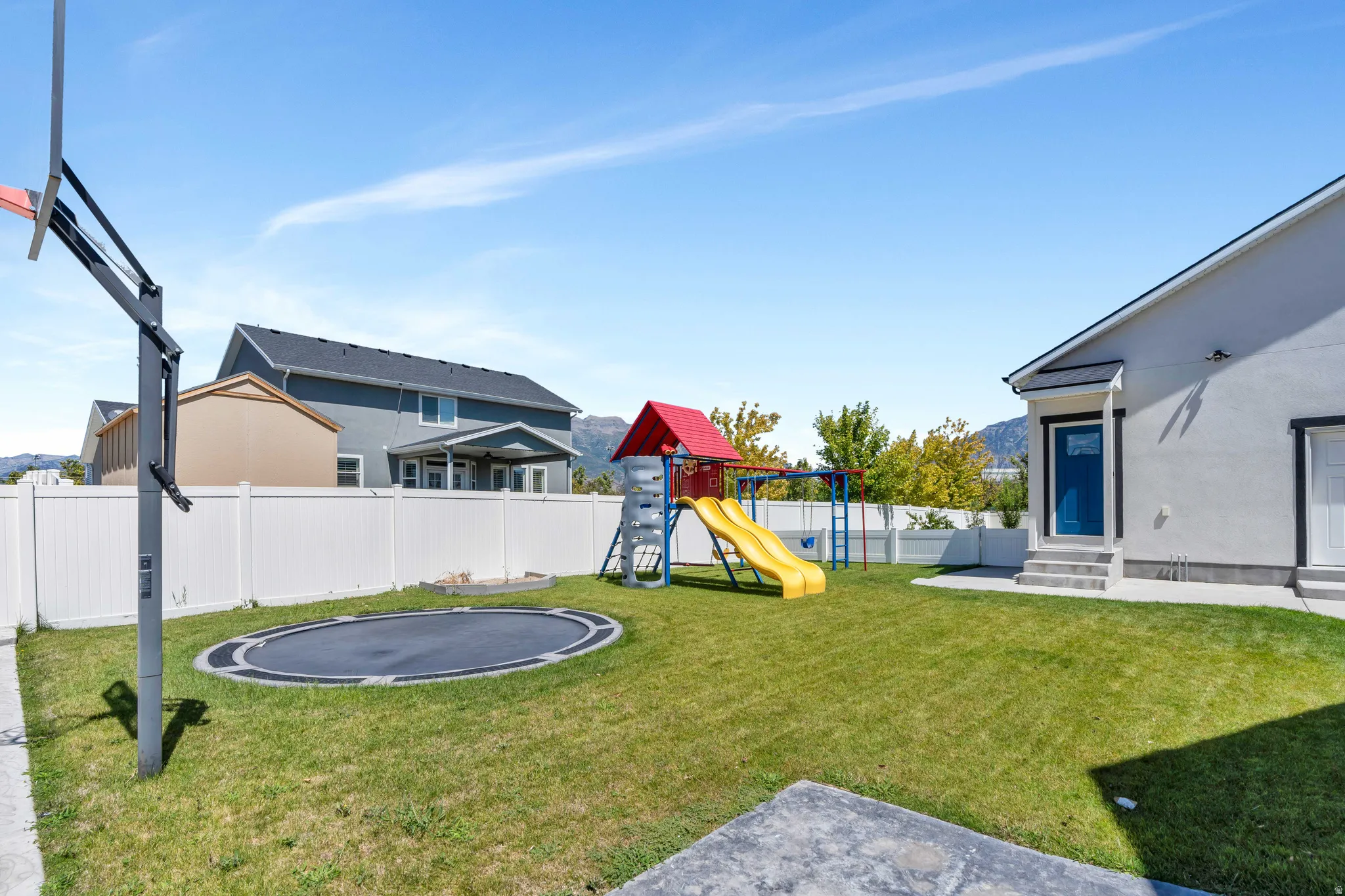 Fenced backyard with a trampoline, a playground, a patio, and entry steps