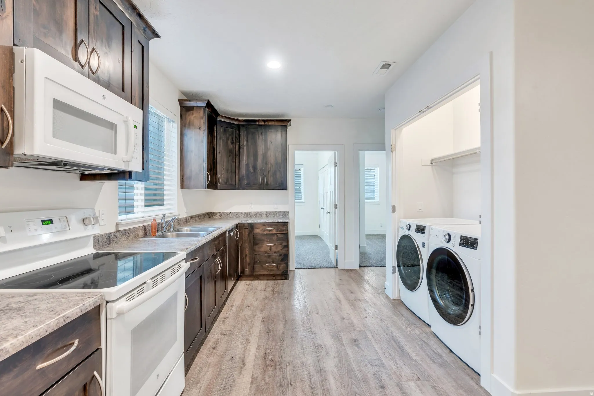 Kitchen with dark wood finish cabinets, white appliances, independent washer and dryer, light countertops, and light wood-type flooring