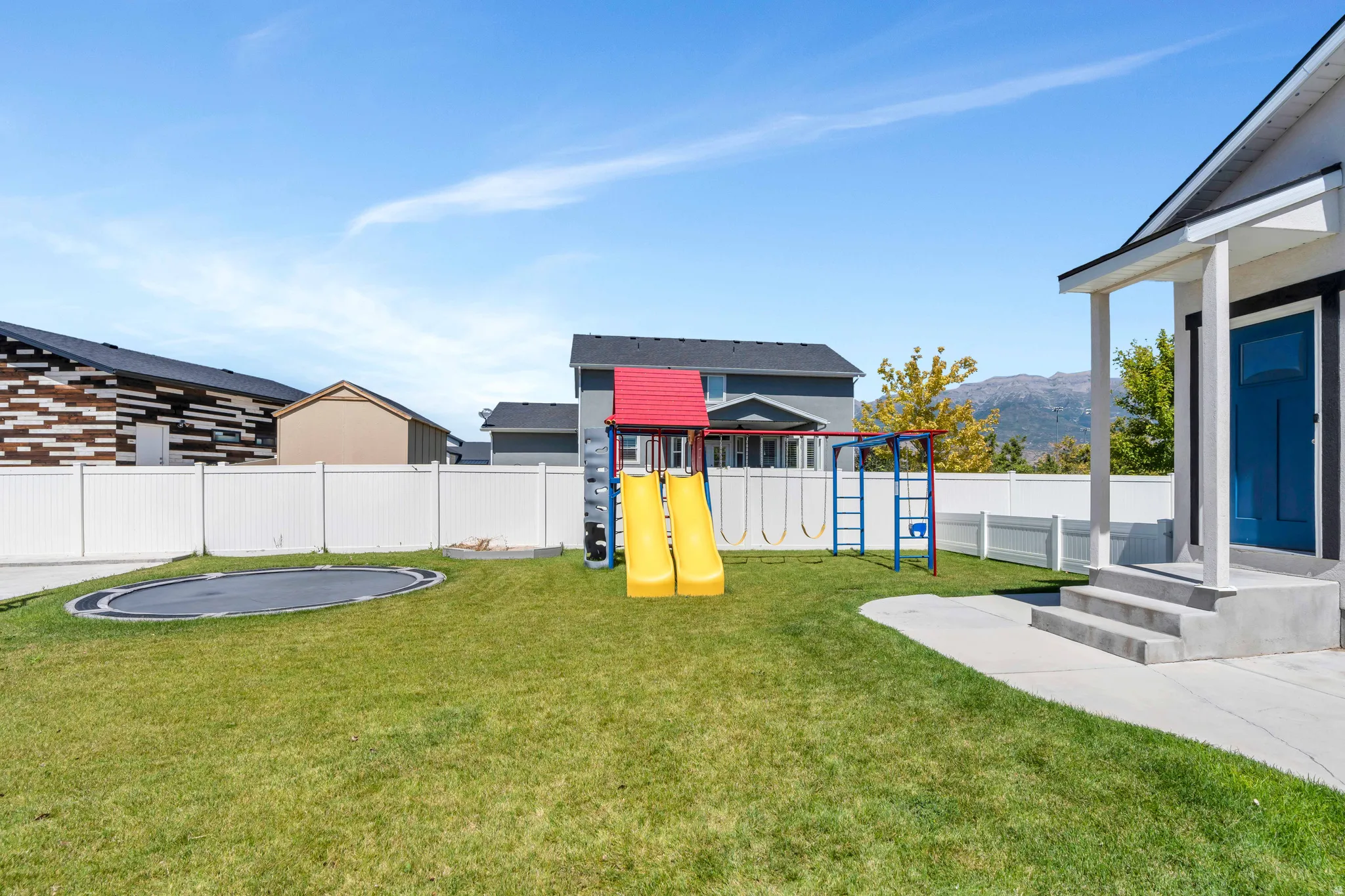 Fenced backyard with a trampoline, a playground, and a mountain view
