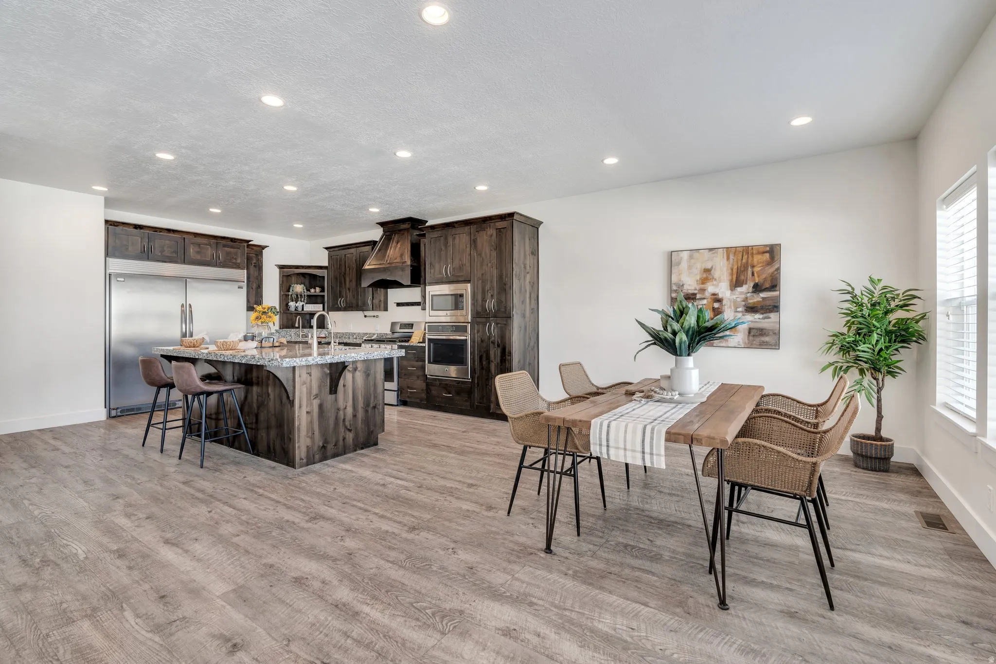 Kitchen with dark wood finish cabinets, a breakfast bar area, built in appliances, light stone countertops, and a kitchen island with sink