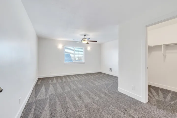 Unfurnished bedroom featuring carpet, a spacious closet, and ceiling fan