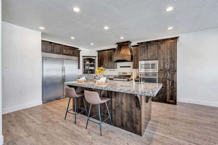 Kitchen featuring dark wood finish cabinetry, built in appliances, light stone countertops, a kitchen island with sink, and recessed lighting
