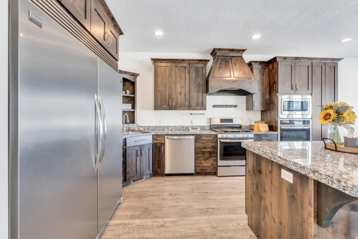 Kitchen with built in appliances, light stone counters, recessed lighting, light wood-type flooring, and dark wood finish cabinets
