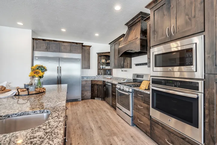 Kitchen featuring built in appliances, dark wood finish cabinets, light stone counters, open shelves, and a textured ceiling