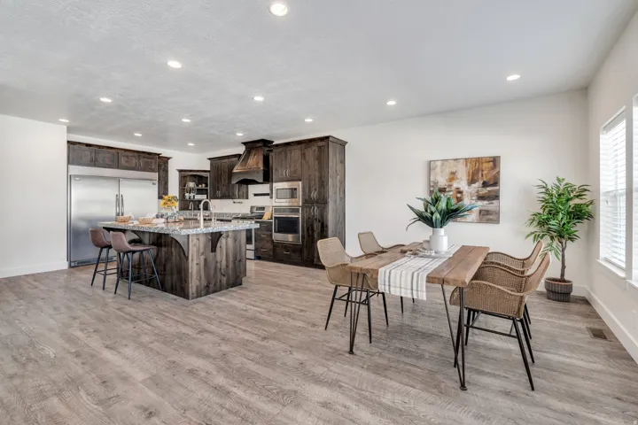 Kitchen with dark wood finish cabinets, a breakfast bar area, built in appliances, light stone countertops, and a kitchen island with sink