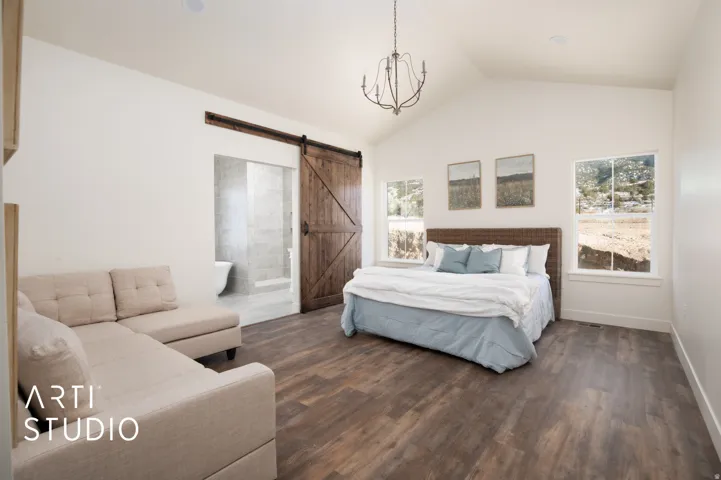 Bedroom featuring a barn door, multiple windows, dark wood finished floors, and ensuite bath