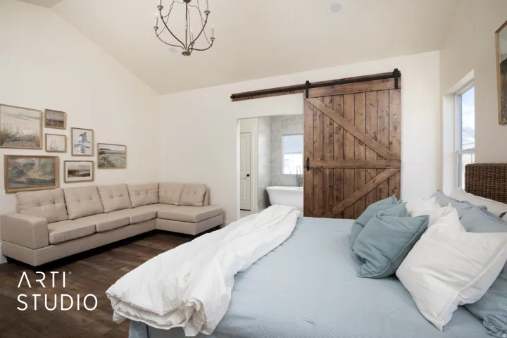 Bedroom with a barn door, wood finished floors, vaulted ceiling, and connected bathroom