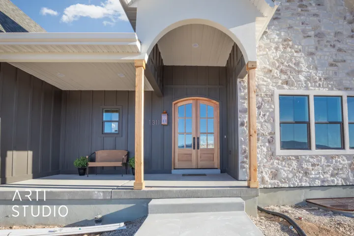 Entrance to property featuring stone siding, french doors, a porch, and board and batten siding