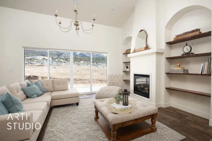 Living room with built in shelves, wood finished floors, a large fireplace, hanging lights, and lofted ceiling