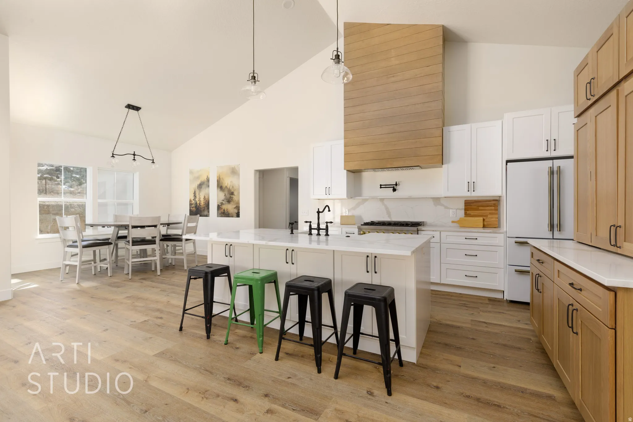 Dual tone kitchen with decorative light fixtures, a kitchen island with sink, high end fridge, two tone color scheme, and lofted ceiling