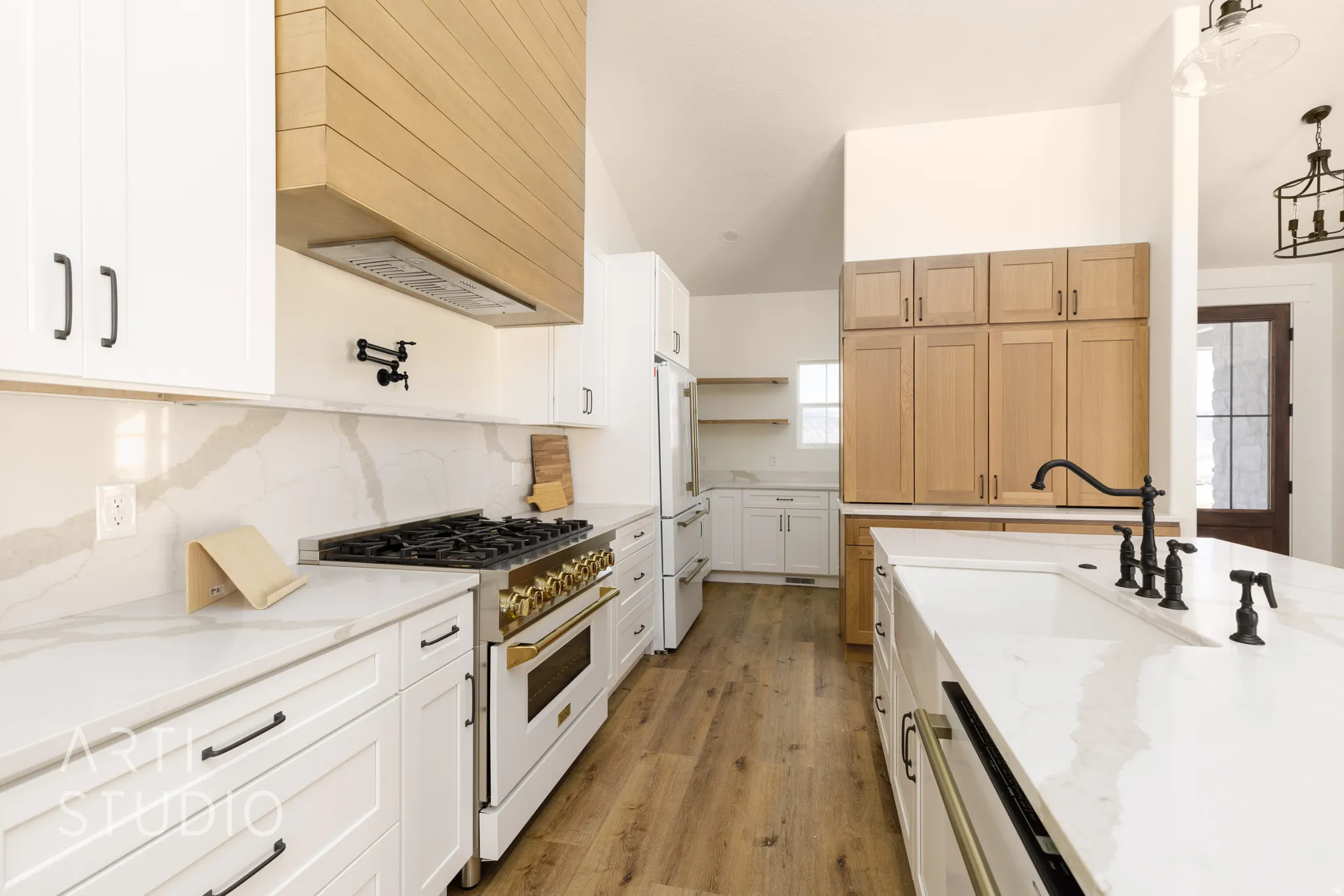Kitchen featuring premium appliances, light stone countertops, light wood-style flooring, decorative backsplash, and decorative light fixtures
