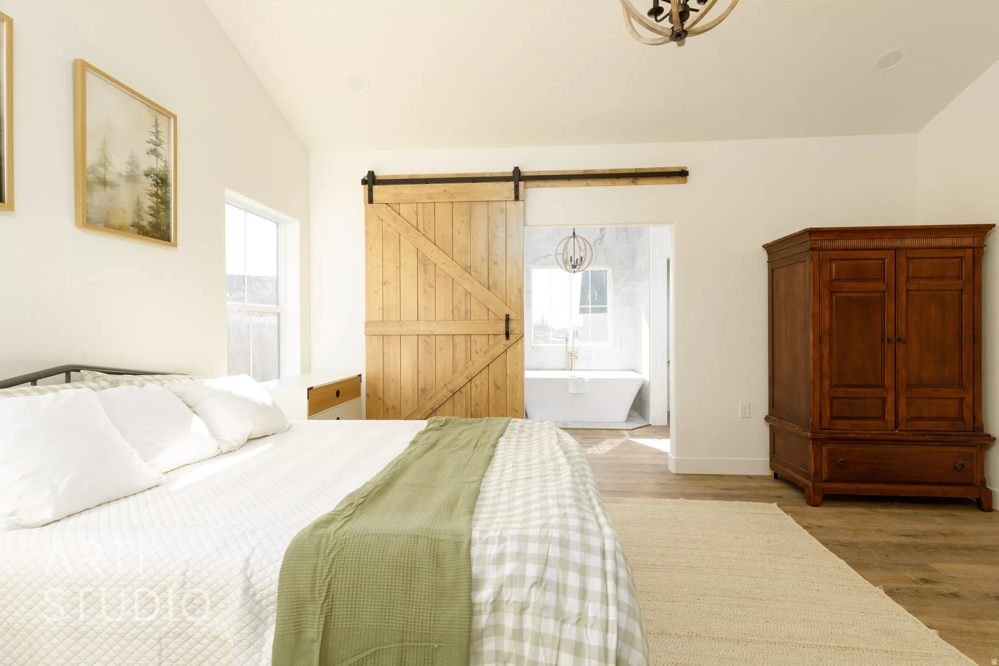 Bedroom with multiple windows, wood finished floors, lofted ceiling, a barn door, and connected bathroom