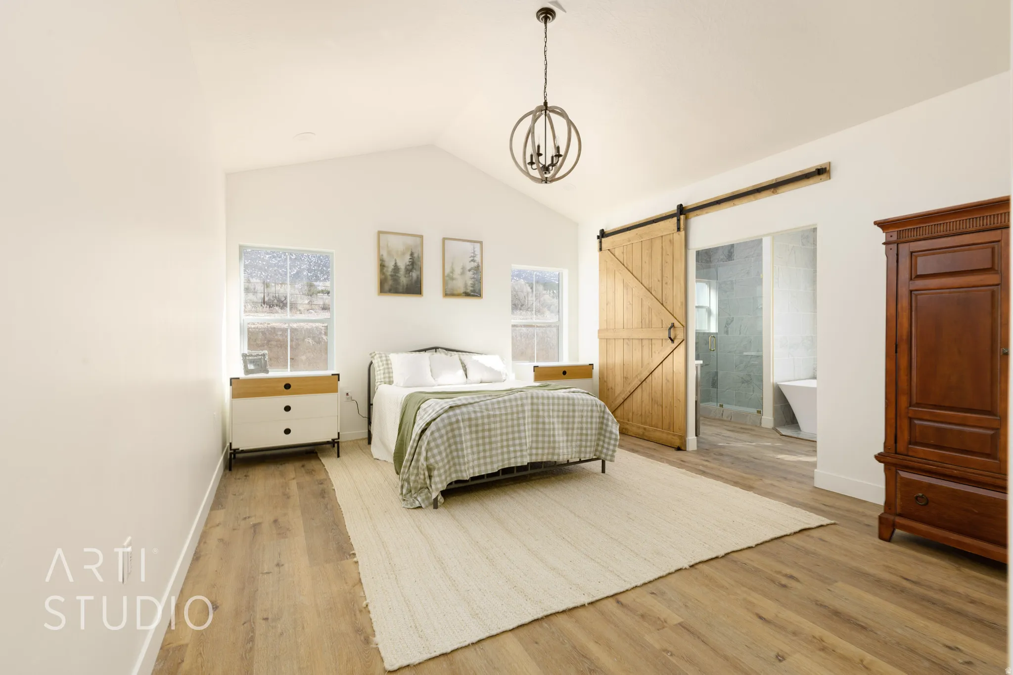 Bedroom with wood finished floors, ensuite bath, a barn door, and suspended lighting