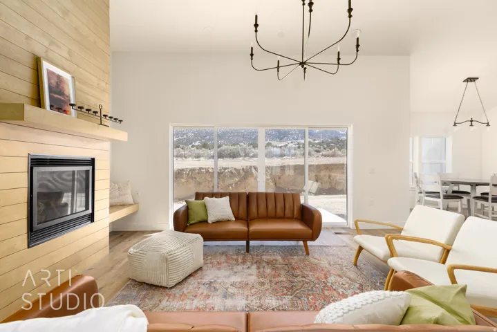 Living room with suspended lighting, a large fireplace, wood finished floors, a high ceiling, and healthy amount of natural light