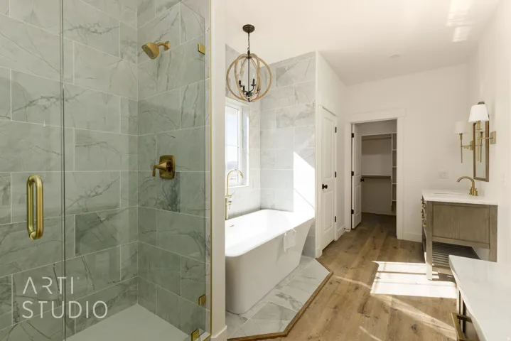 Full bath with vanity, a freestanding bath, a spacious closet, a stall shower, and wood finished floors