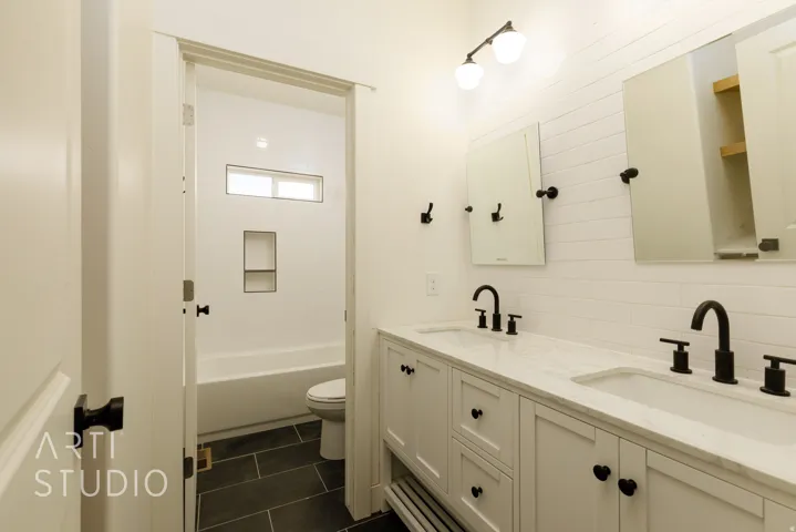 Full bath with double vanity, dark tile patterned floors, shower / bath combination, and decorative backsplash