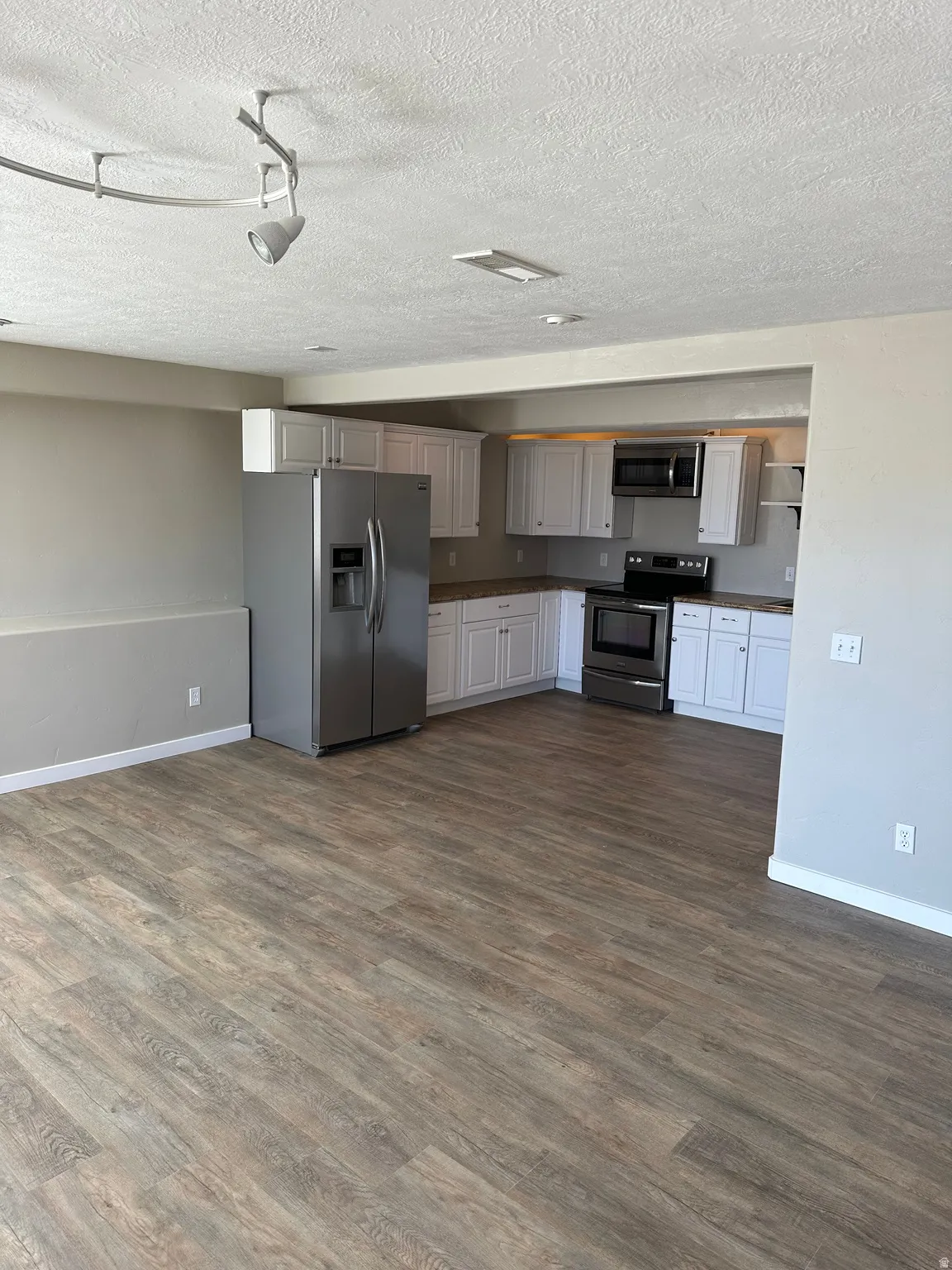 Kitchen with stainless steel appliances, white cabinets, wood finished floors, a textured ceiling, and track lighting