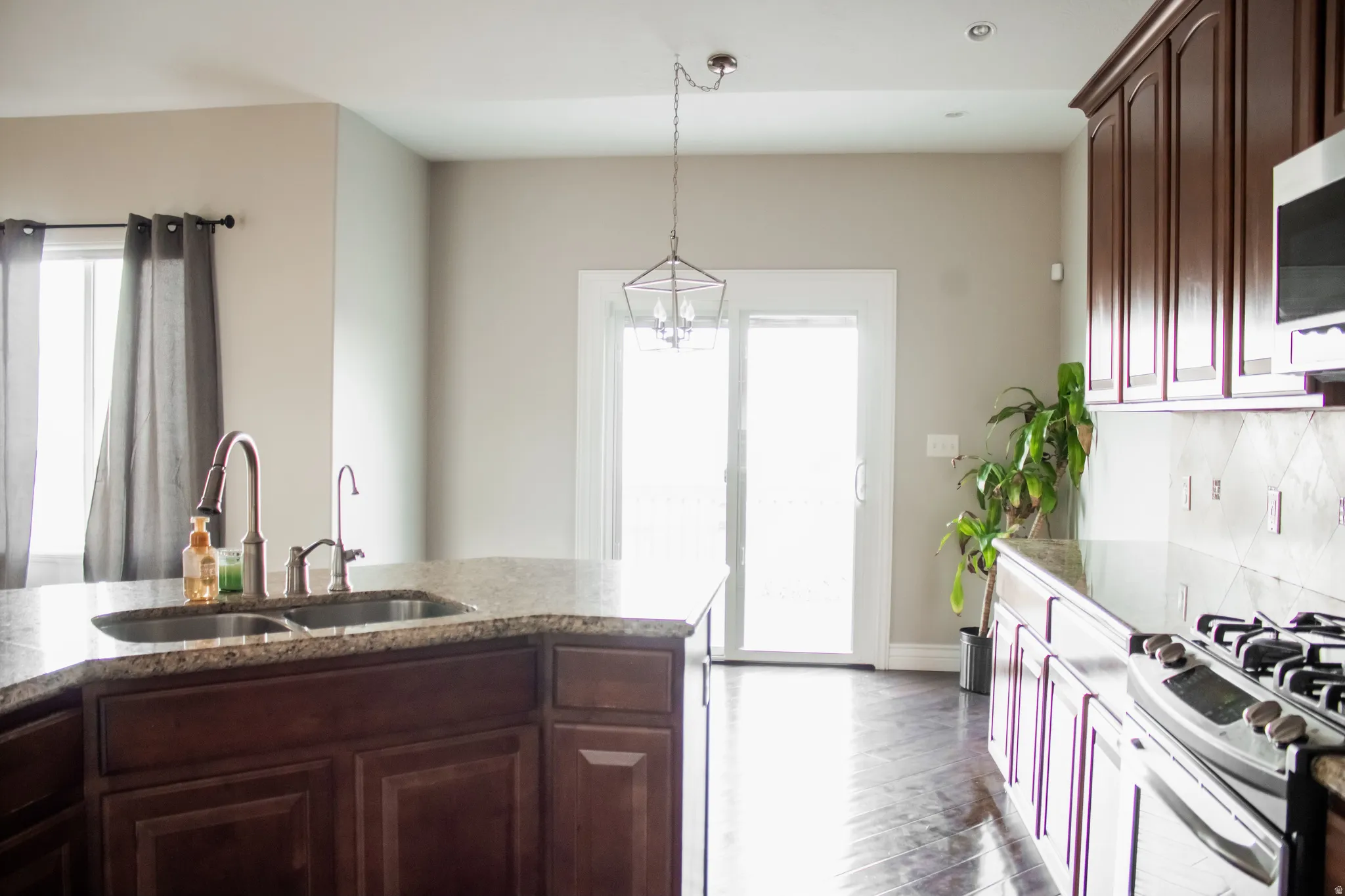 Kitchen with hanging light fixtures, dark brown cabinetry, dark wood finished floors, appliances with stainless steel finishes, and dark stone countertops