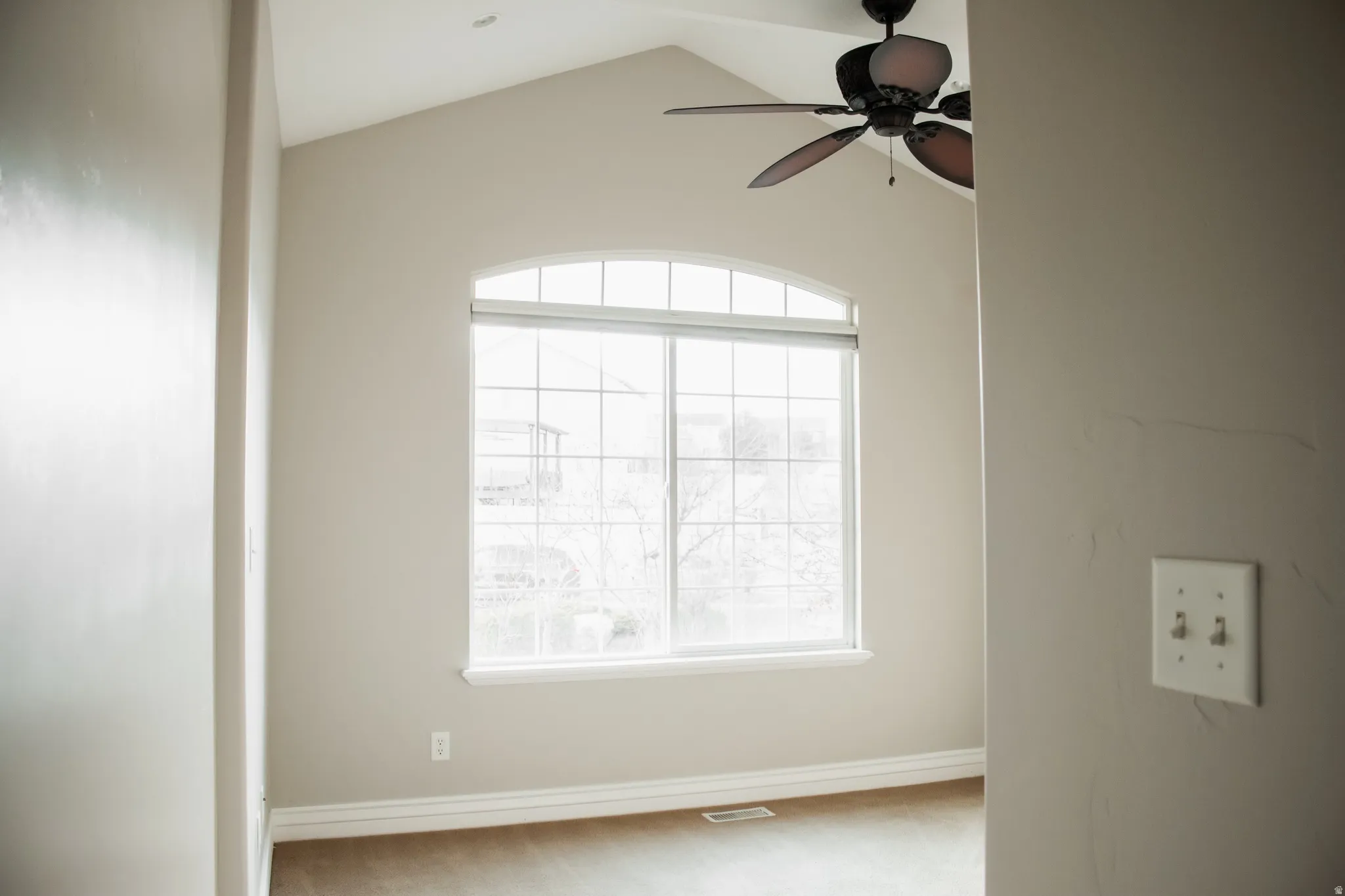 Carpeted bedroom with a large window, ceiling fan, and vaulted ceiling