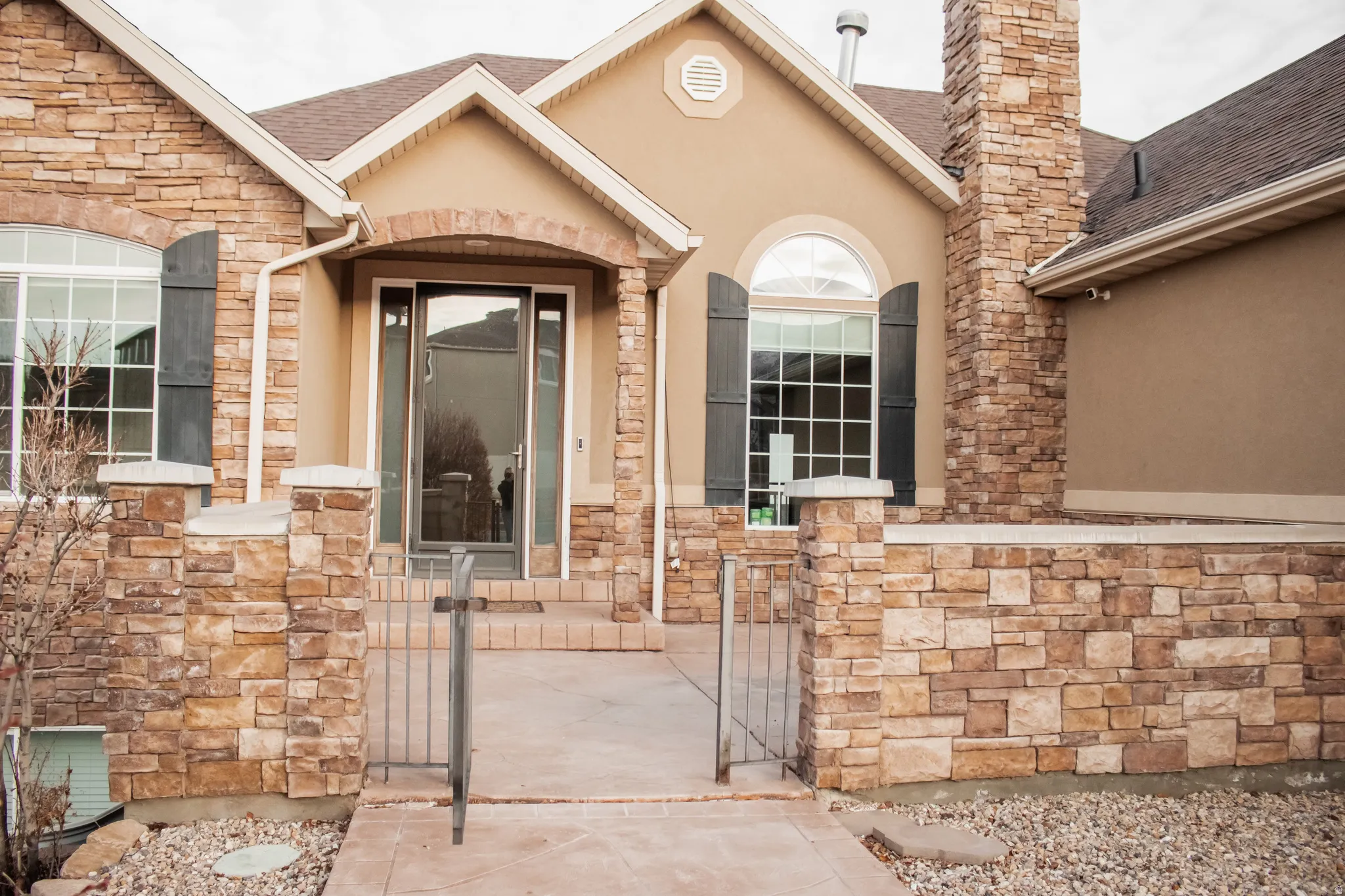 Property entrance featuring stucco siding, stone siding, a gate, and roof with shingles