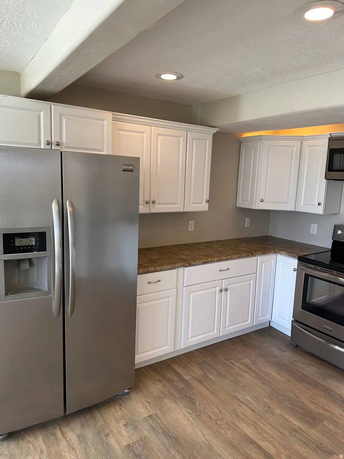 Kitchen featuring a textured ceiling, appliances with stainless steel finishes, white cabinets, dark wood-type flooring, and dark stone counters