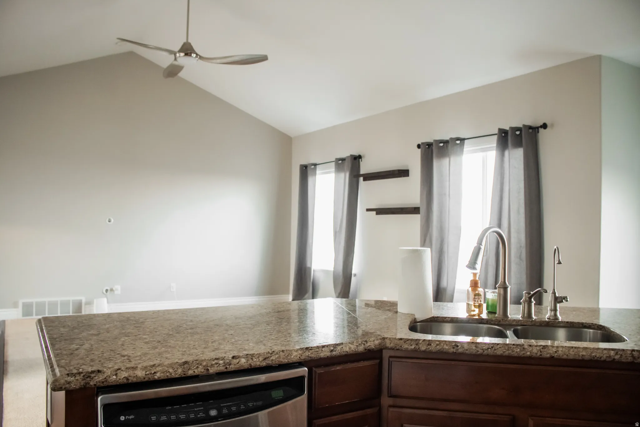Kitchen island with dark brown cabinets, stainless steel dishwasher, plenty of natural light, and vaulted ceiling