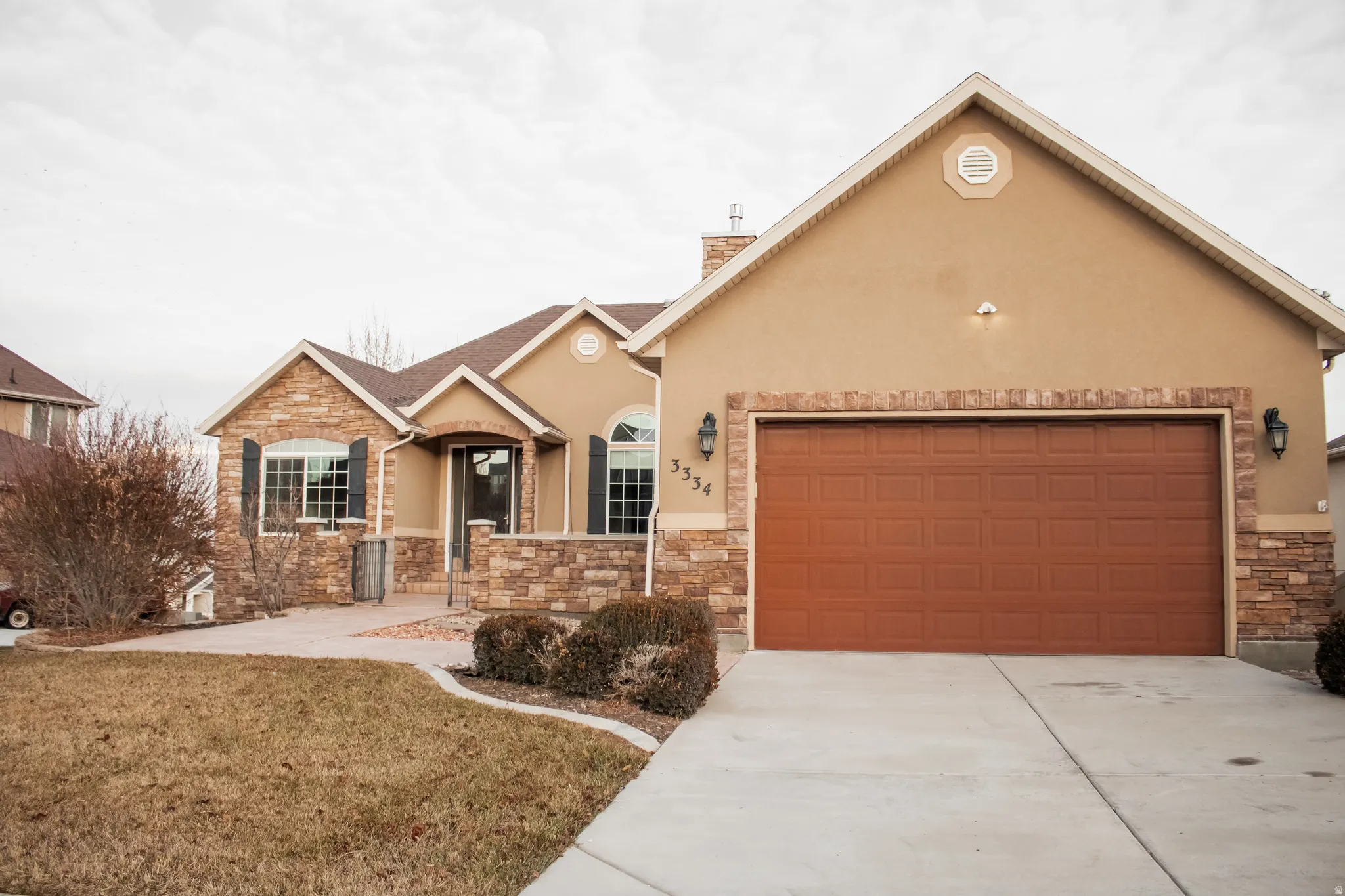 View of front facade featuring stone siding, a front yard, concrete driveway, stucco siding, and a garage
