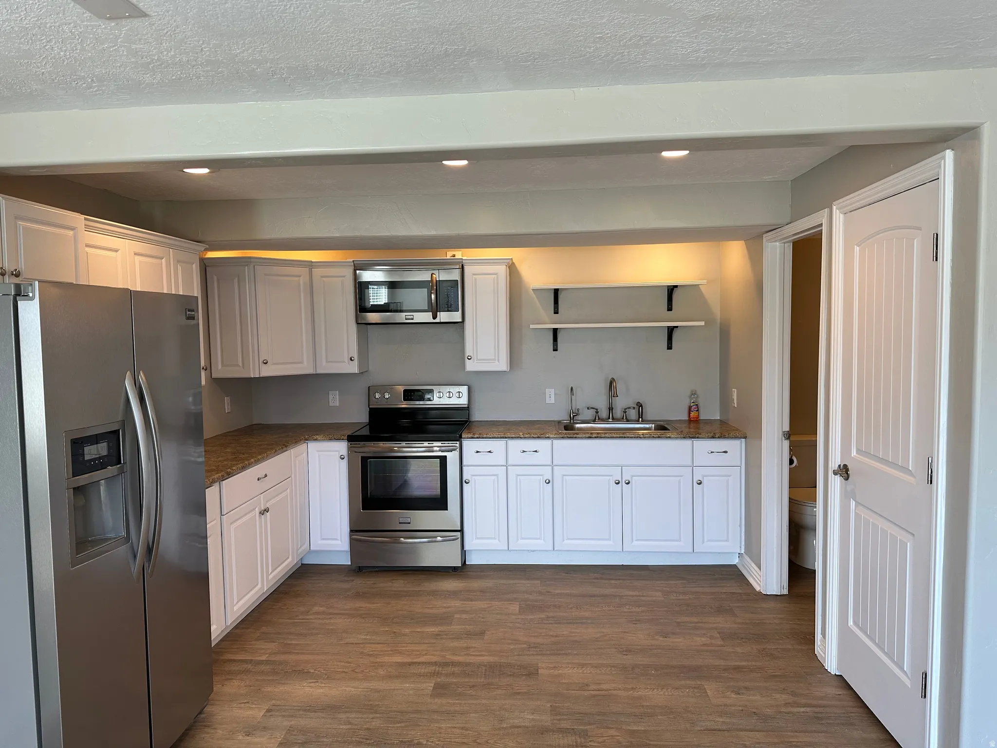 Kitchen with stainless steel appliances, white cabinets, dark wood-style floors, open shelves, and a textured ceiling