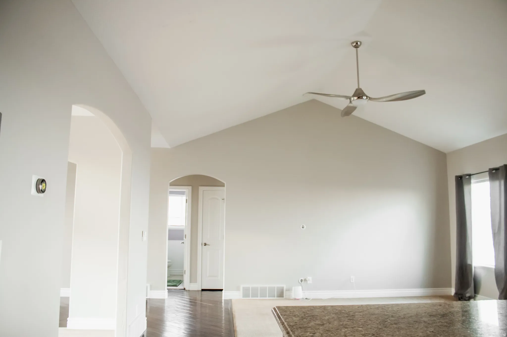 Living room featuring arched walkways, wood finished floors, high vaulted ceiling, and ceiling fan