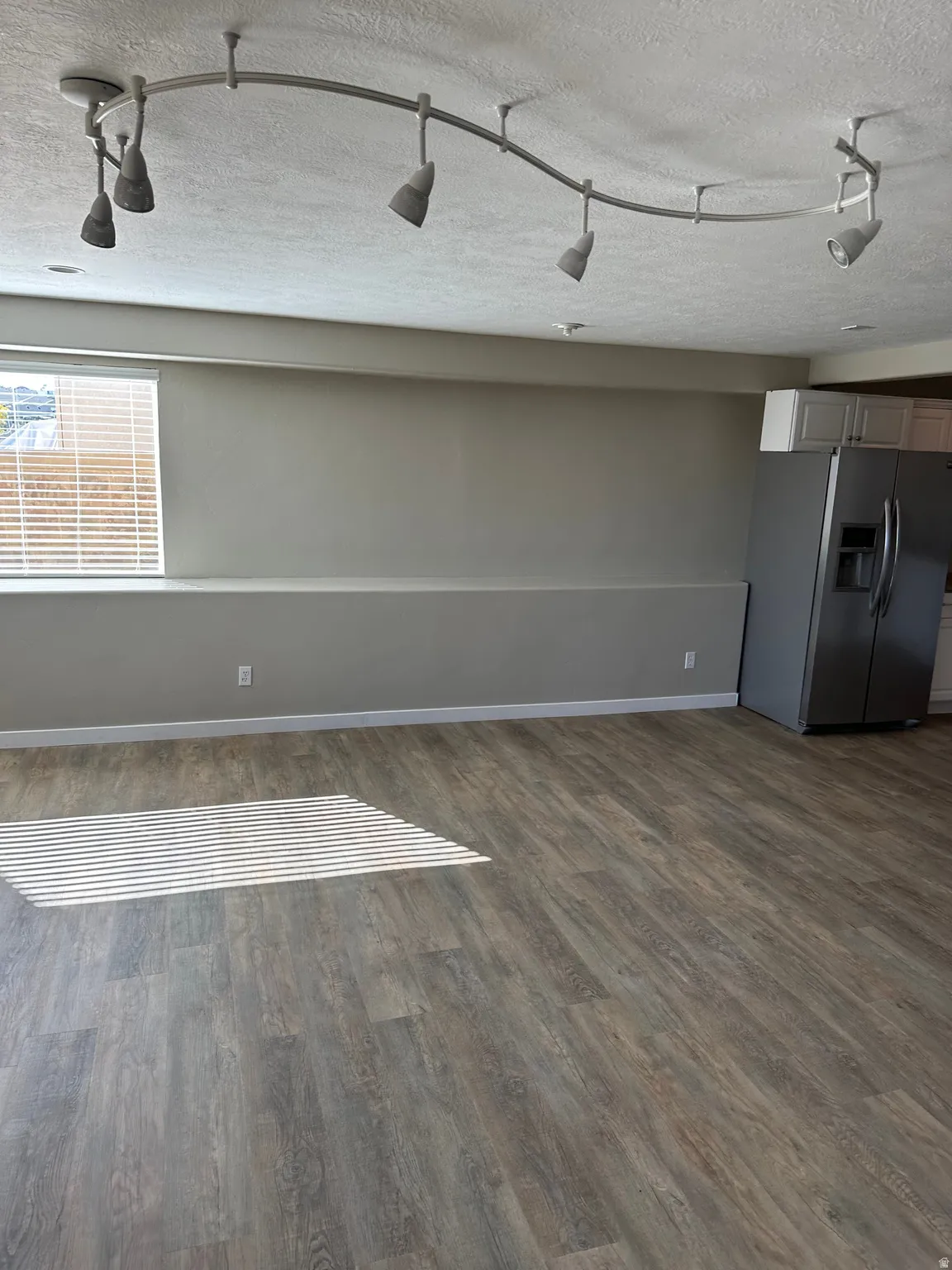 Unfurnished living room featuring track lighting and wood-style flooring.