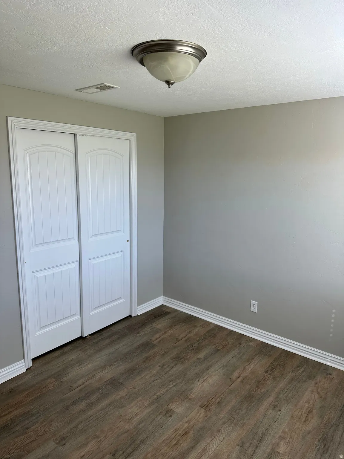 Bedroom with dark wood-style floors, a textured ceiling, and a closet